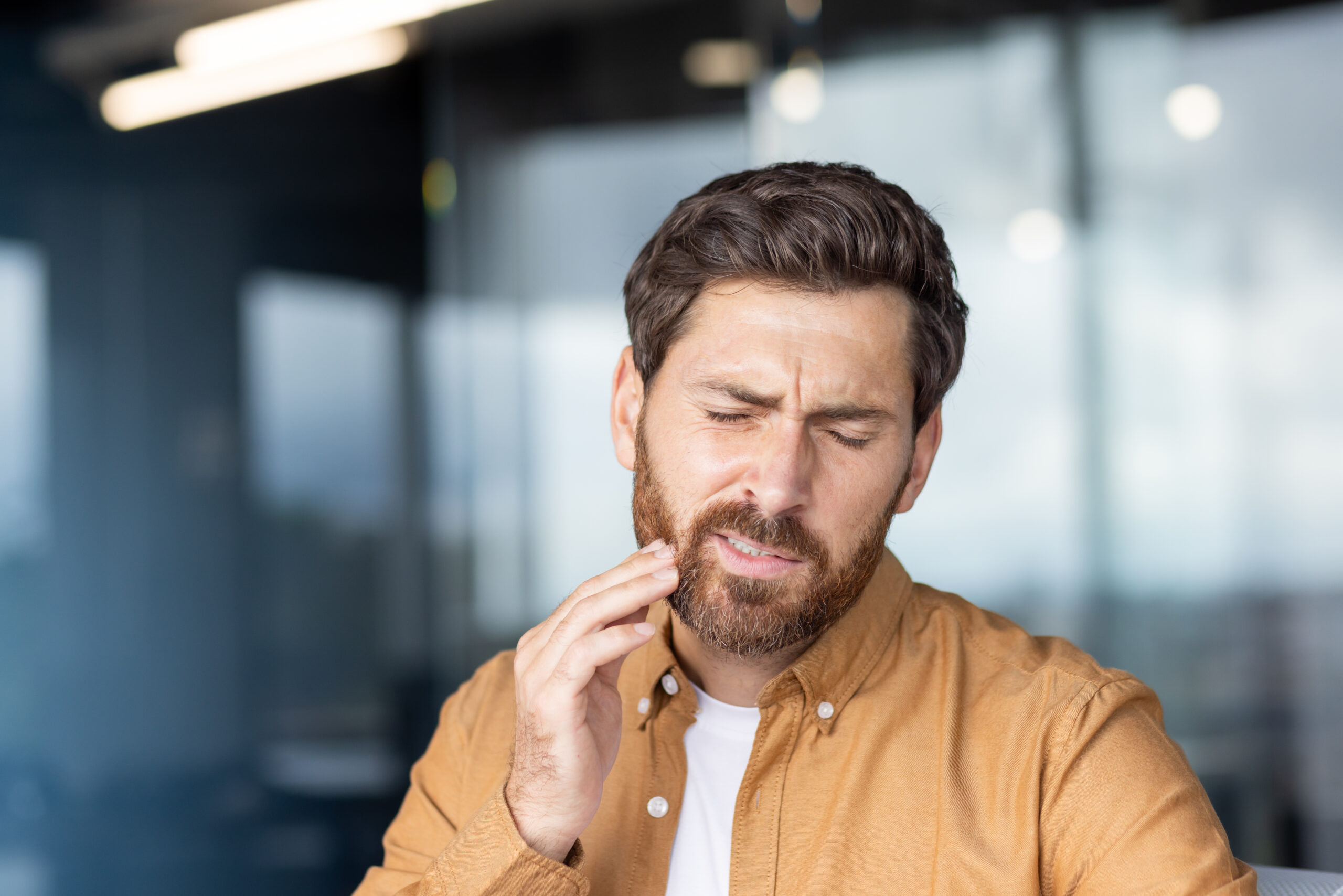 Young man experiencing an acute toothache or dental pain, touching his jaw with a hand, depicting discomfort, dental problems, and the need for urgent dental care or treatment