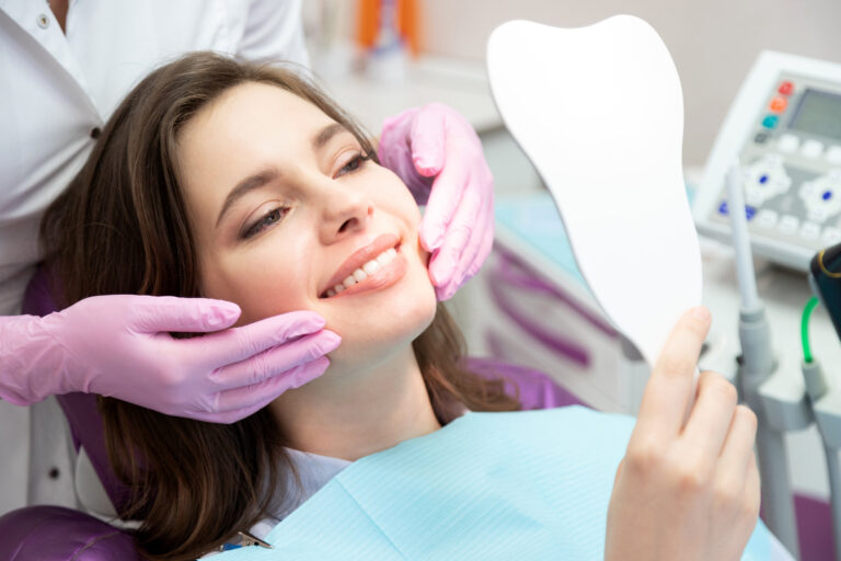 Happy patient after tooth treatment at dental clinic. Smiling girl with white well-groomed teeth after taking doctor help. Satisfied lady look at mirror enjoy healthy enamel after whitening procedure