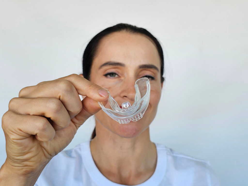 Smiling woman holds transparent plastic mouth guard in her hand