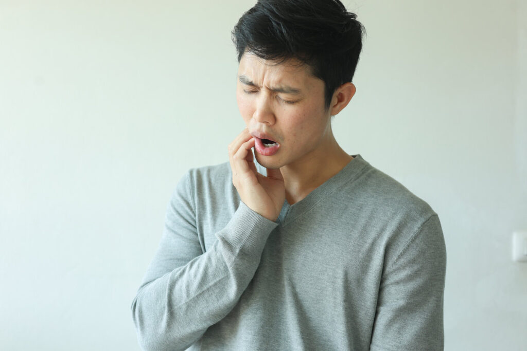 close up young asian man frown and use hand to massage on cheek after feeling pain or hurt from tmj muscle symptom at home for un healthy lifestyle and treatment concept
