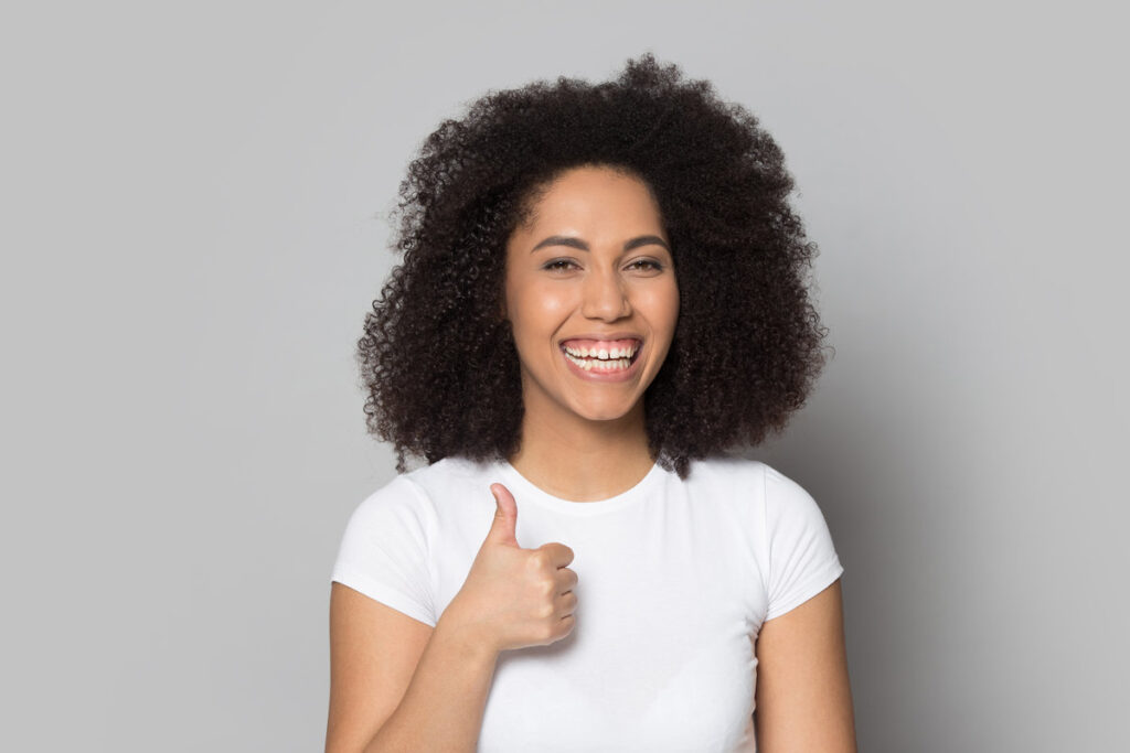 Smiling african American young woman isolated on grey studio background show thumbs up recommend good service, happy biracial millennial girl look at camera laughing give sincere recommendation