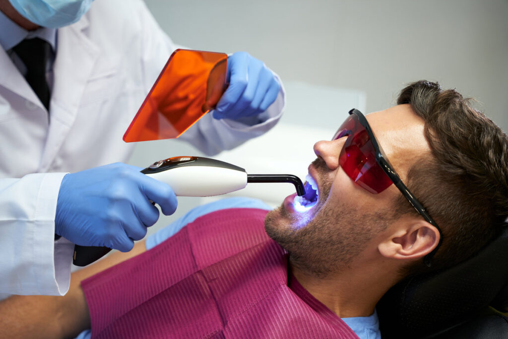 Young man in glasses sitting in dental chair with his mouth open while receiving laser treatment