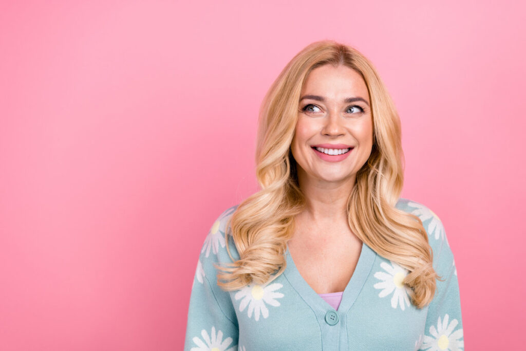 Photo of positive cheerful woman with wavy hairdo dressed print cardigan look at sale empty space isolated on pink color background.
