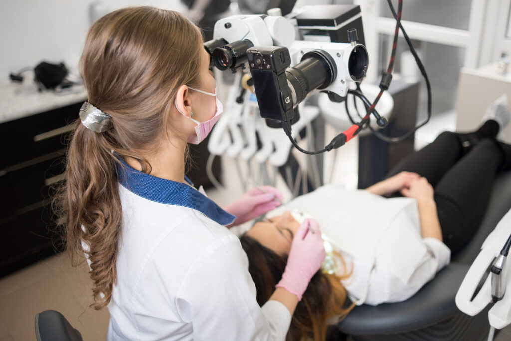 Female dentist with dental tools - microscope, mirror and probe checking up patient teeth at dental clinic office. Medicine, dentistry and health care concept. Dental equipment