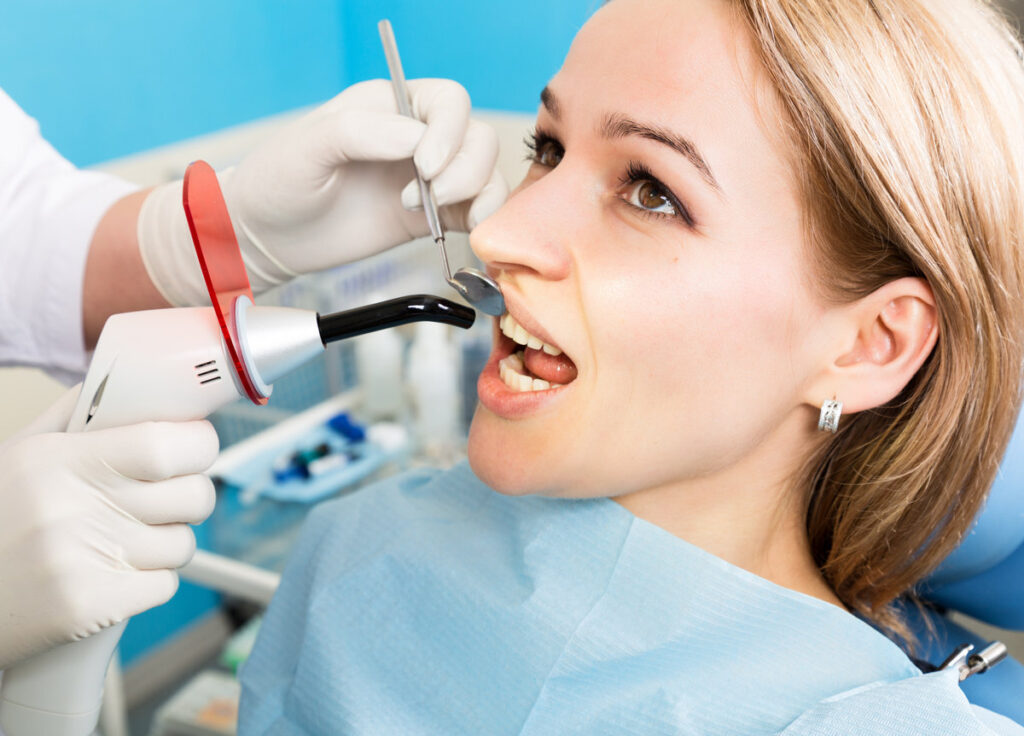 The reception was at the female dentist. Doctor examines the oral cavity on tooth decay. Caries protection. Tooth decay treatment. Dentist working with dental polymerization lamp in oral cavity.