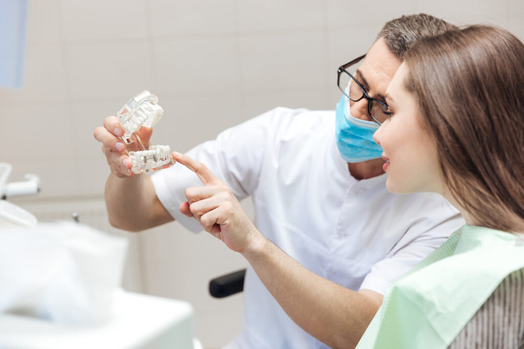 Man dentist show dentures teeth at dental surgery to his patient at the clinic