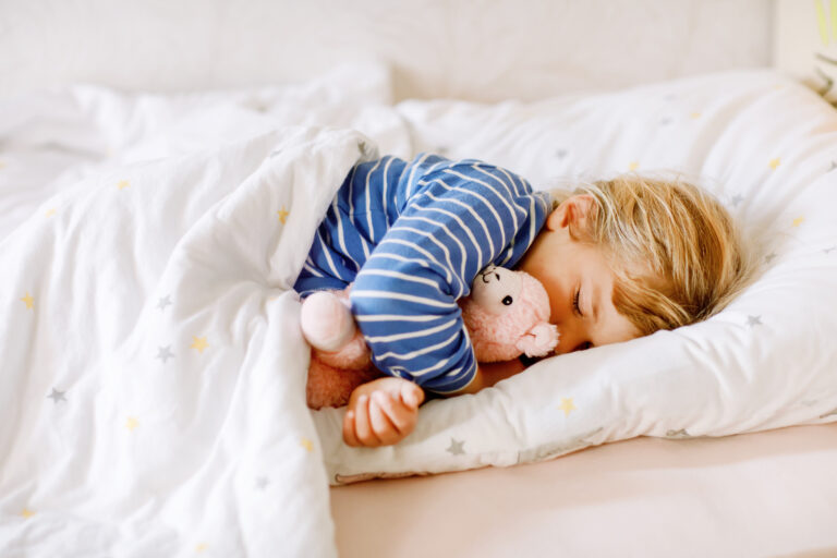 Toddler sleeping peacefully in bed with a soft toy