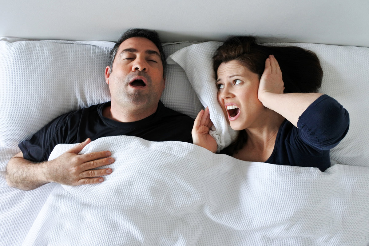 Woman (age 30-40) suffers from her partner (age 35 - 45) snoring in bed. Couple lifestyle and people health care concept. Real people copy space