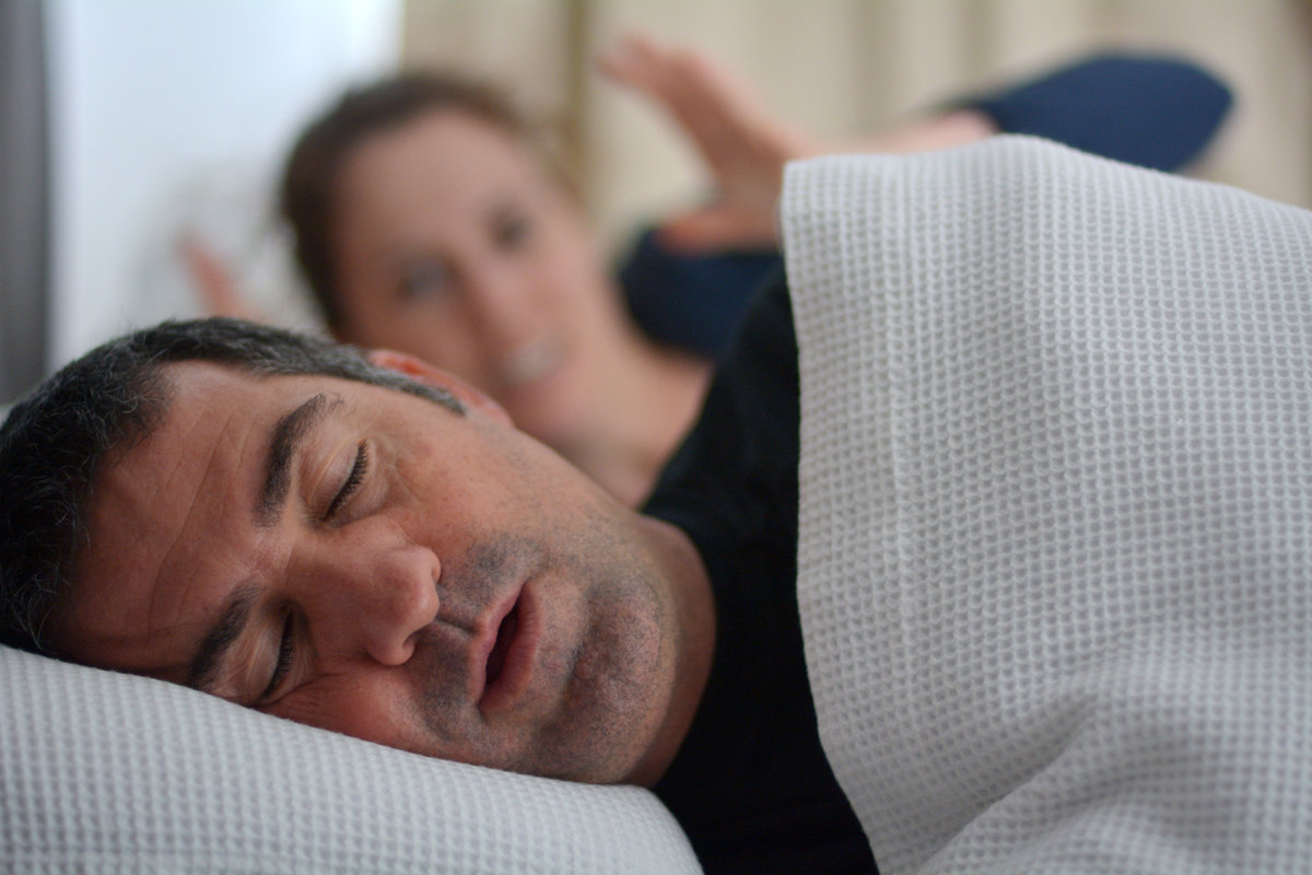 Woman (age 30) suffers from her male partner (age 40) snoring in bed. Noise concept. Real people. Copy space